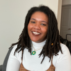 Picture of a young black women with dreads, smiling and wearing a long sleeve white turtle neck